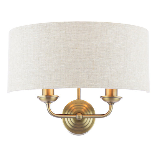 Antique brass wall light with two arms and natural shade on white background.