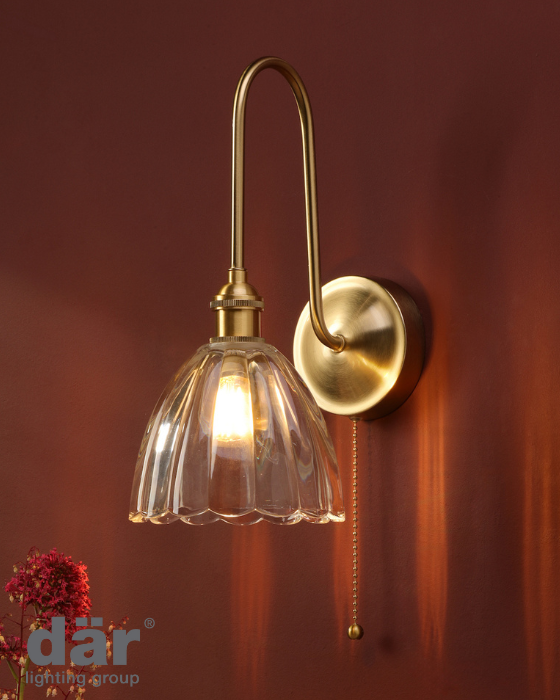 Wall-mounted gold light fixture with clear scalloped glass shade and pull cord switch on a deep red background.
