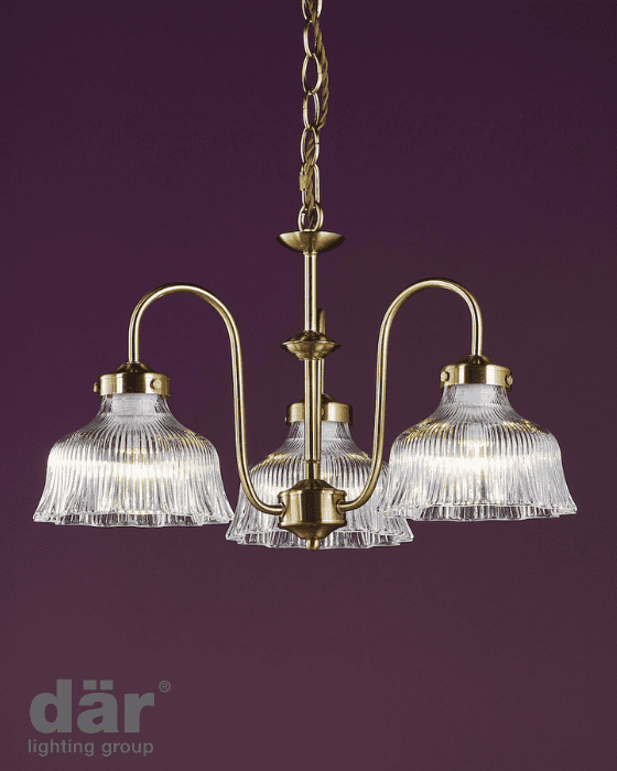 Chandelier with three clear glass shades and gold metal fixtures on a purple background, featuring the där lighting group logo.