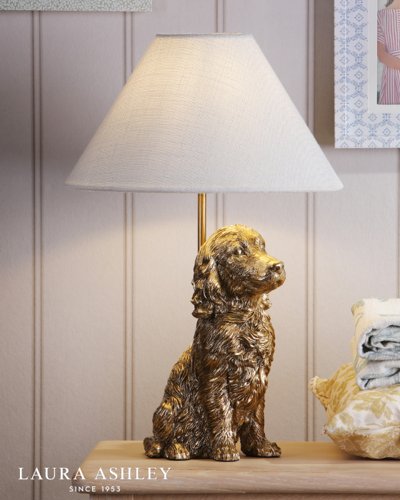 Dog-shaped antique gold table lamp with ivory linen shade on a wooden surface with a neutral background