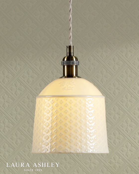 Pendant light with textured cream glass shade and antique brass fitting against a patterned wall, featuring Laura Ashley logo.