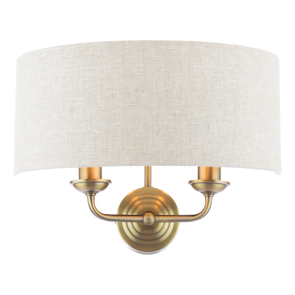 Antique brass wall light with two arms and natural shade on white background.